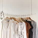 Minimalist clothing rack with branded clothes womens in neutral tones on wooden hangers.