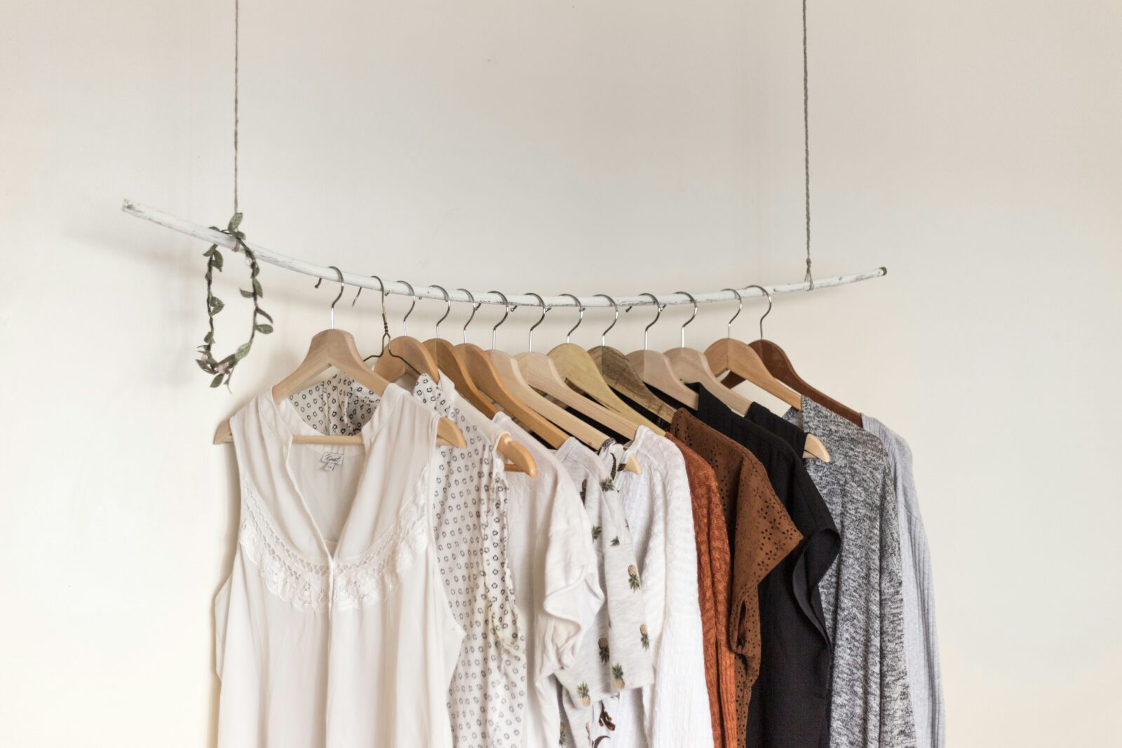Minimalist clothing rack with branded clothes womens in neutral tones on wooden hangers.