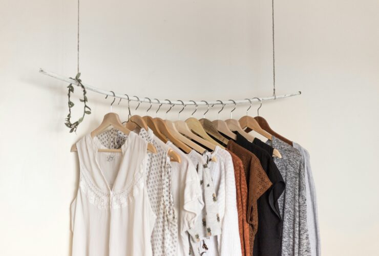 Minimalist clothing rack with branded clothes womens in neutral tones on wooden hangers.