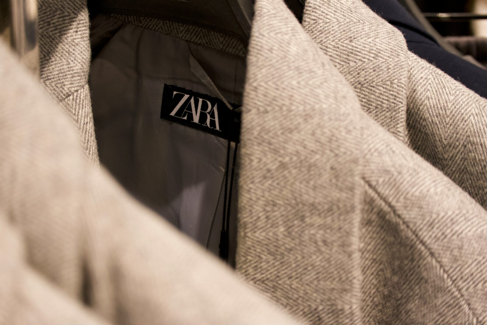 Is Zara fast fashion — close-up of Zara label on tweed jacket in clothing rack
